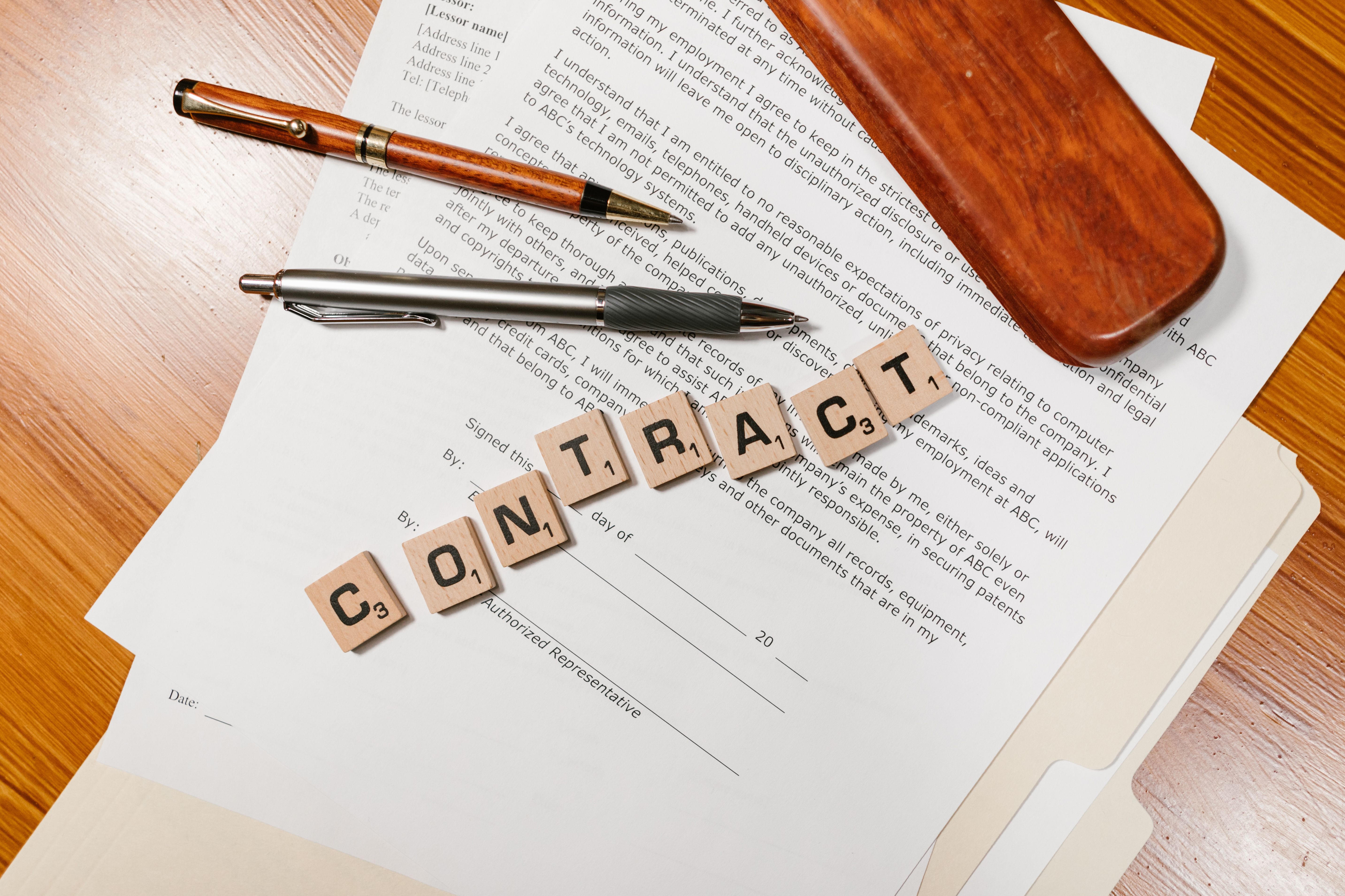 A contract document with pens and wooden letter tiles spelling 'CONTRACT'.